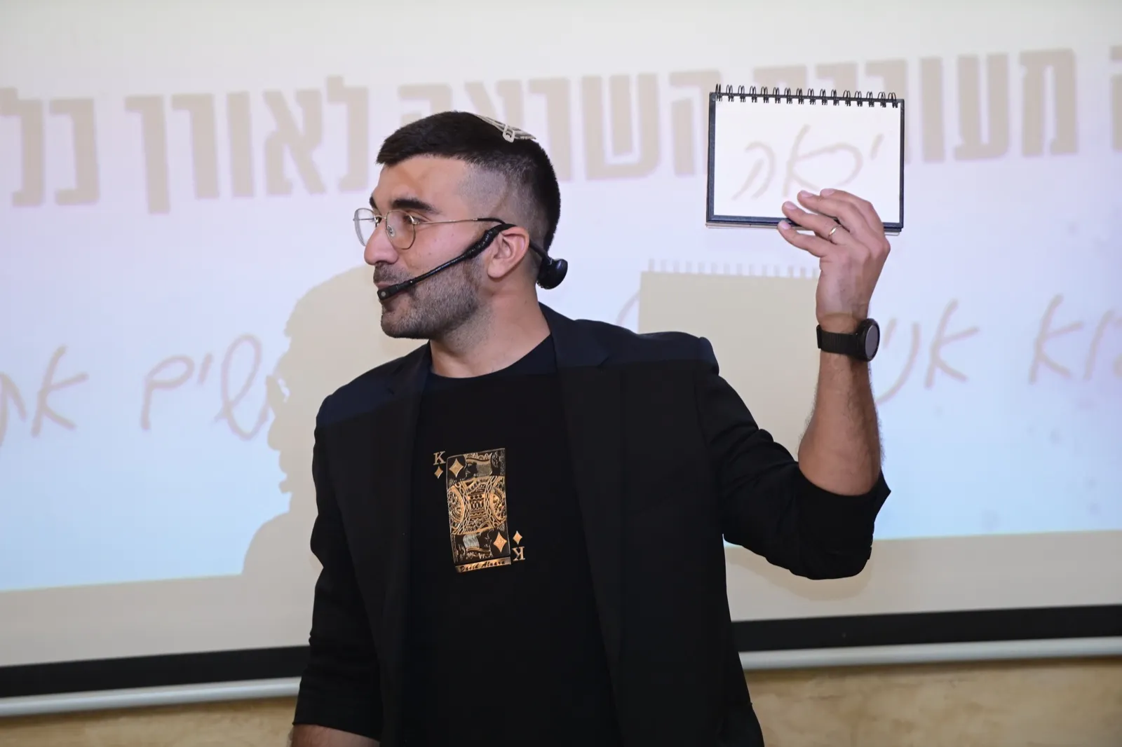 עומרי ביטון על הבמה מחזיק פנקס עם תחזית